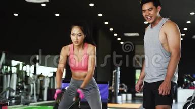 亚洲私人教练指导一名<strong>健美女</strong>子在健身馆进行交叉式绳索练习